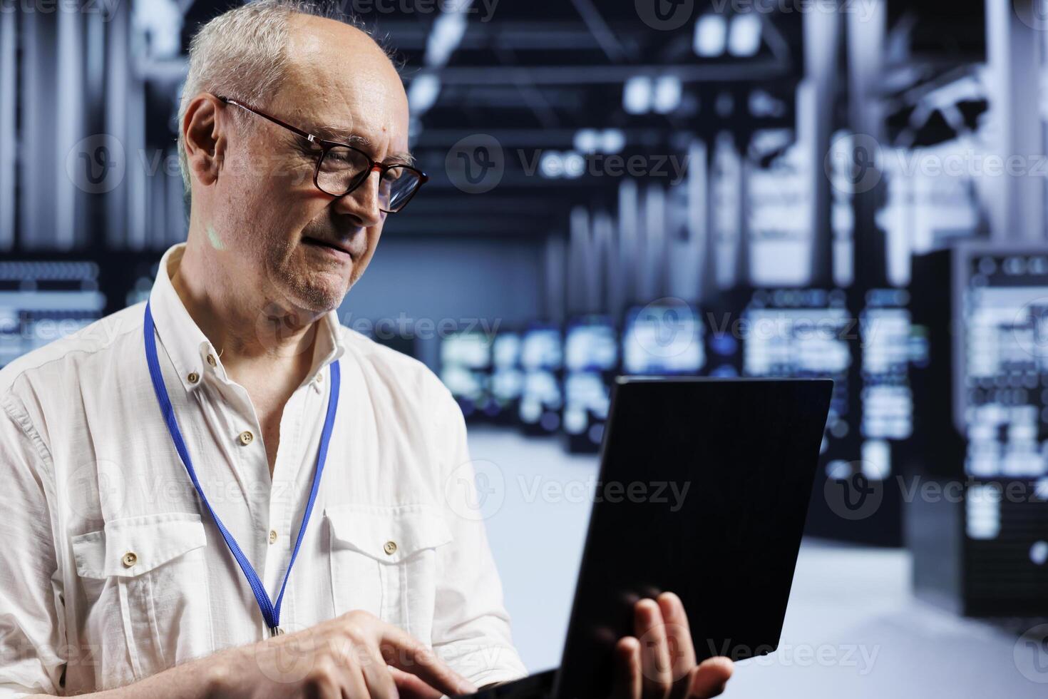 Senescent system administrator inspects server clusters in data center, ensuring smooth performance. Precise professional monitoring energy consumption across units components using laptop photo