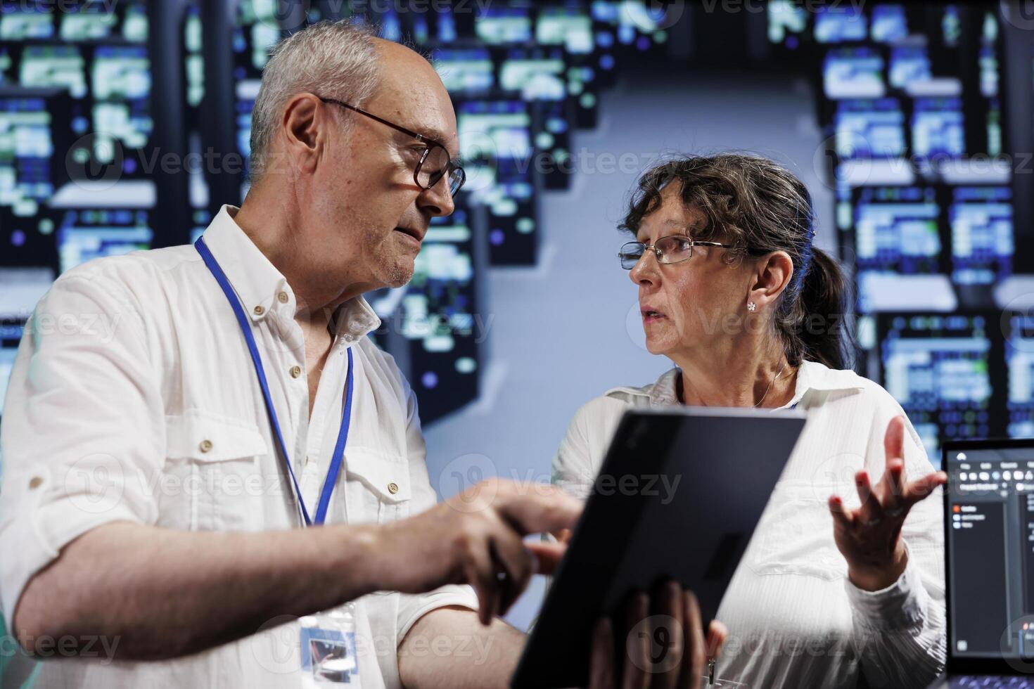 Elderly servicemen running analysis on supercomputers helping businesses manage databases, host websites and store files. Meticulous repairmen auditing high tech server farm electronics photo