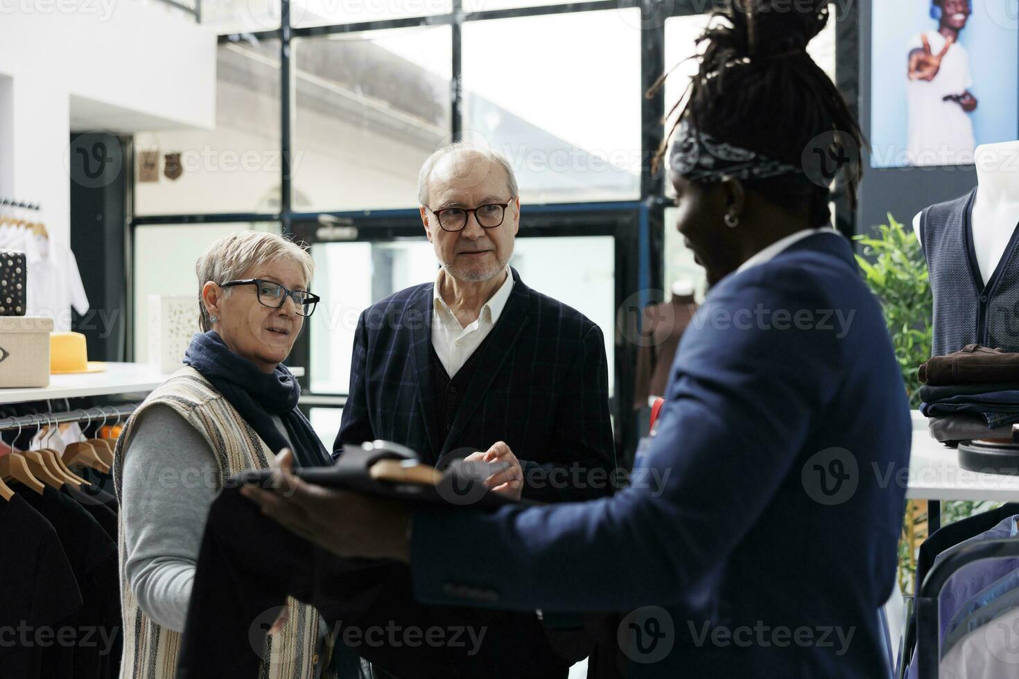 mayor Pareja que se discute camisa tela con sala de exposición obrero, comprando de moda ropa para formal vestir en moderno boutique. mayor hombre mirando a nuevo Moda colección en compras centro. Moda concepto foto