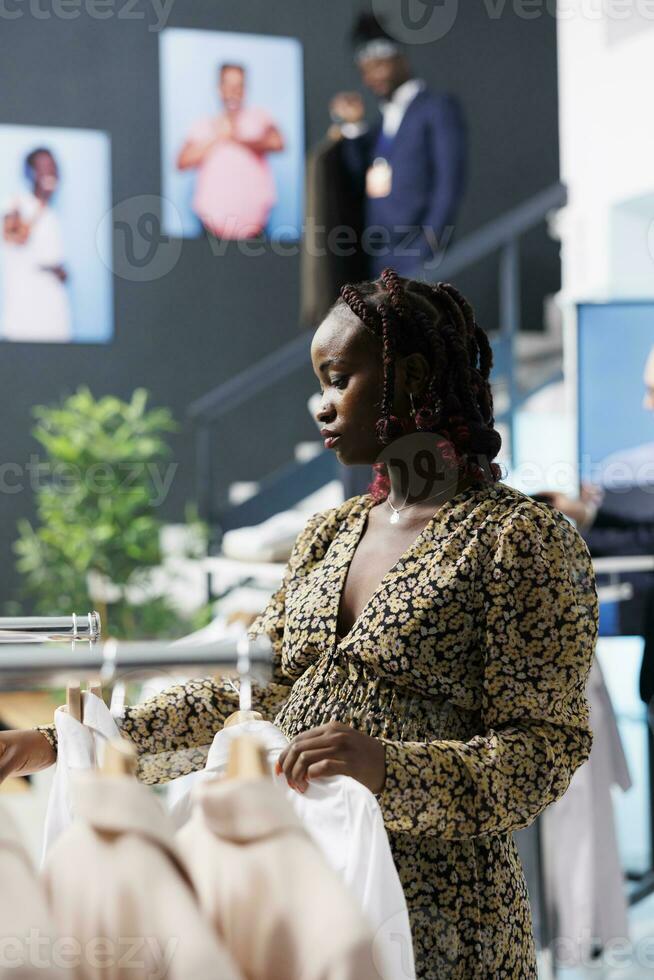 Pregnant customer checking new fashion collection in clothing store, shopping for casual wear. African american woman buying fashionable clothes and accessories during commercial activity. photo