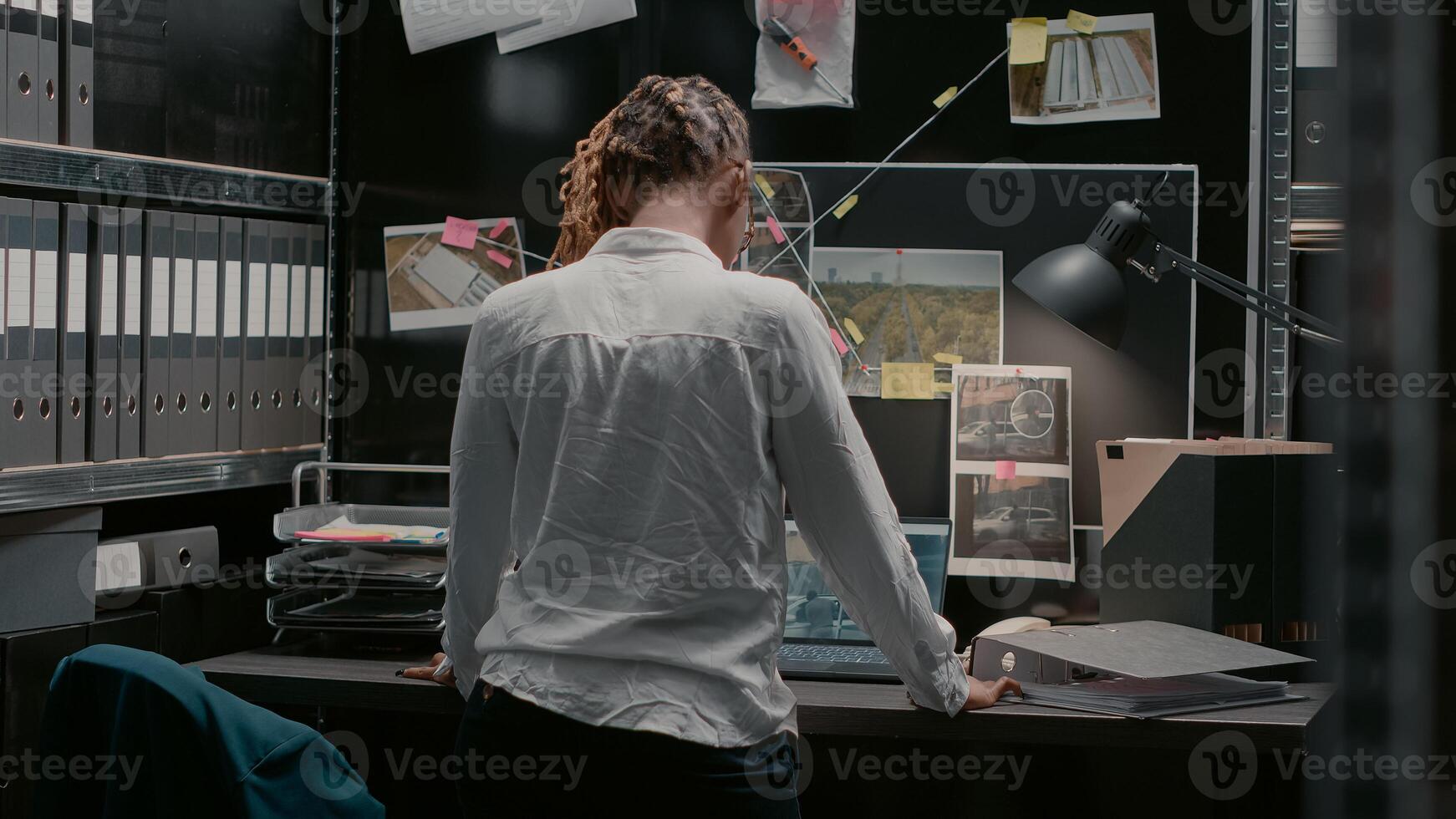 Private investigator examining criminal clues files on map in archive room, reading suspicious information. Law enforcement agent studying forensic evidence to catch crime suspect. photo