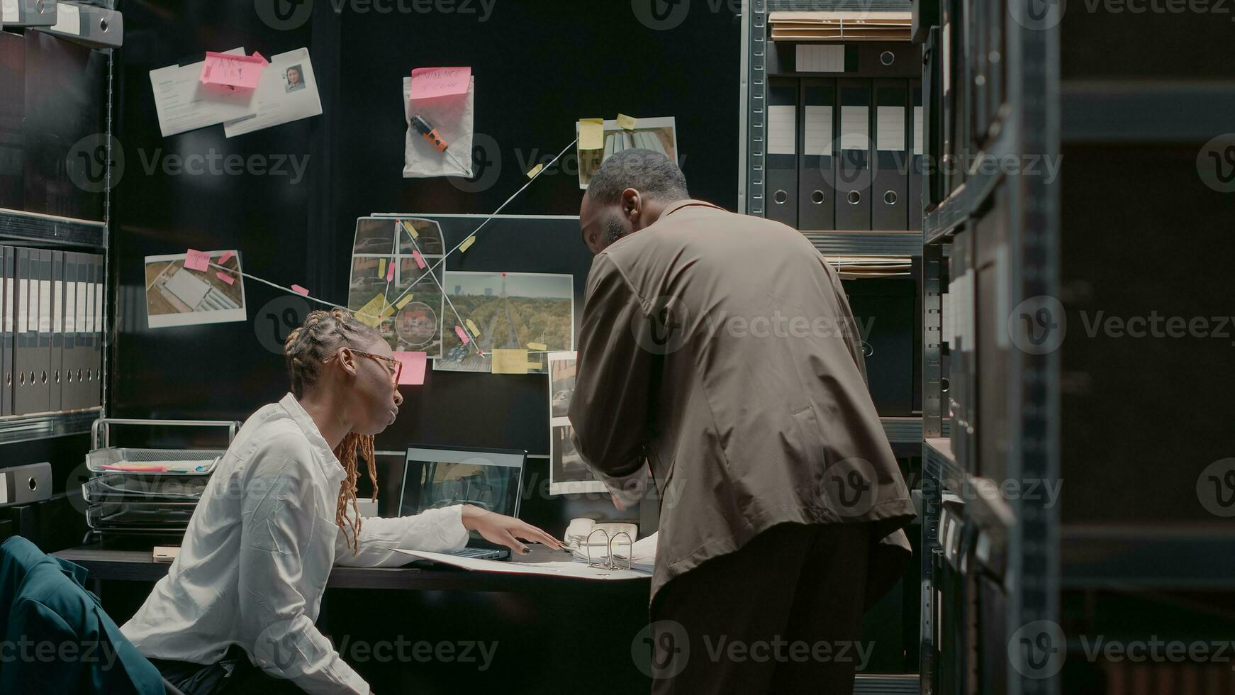 africano americano detectives mirando a fotos en policía archivo, haciendo investigación a resolver delincuente caso. inspectores examinando físico evidencia a descubrir detalles en investigación crimen tablero.