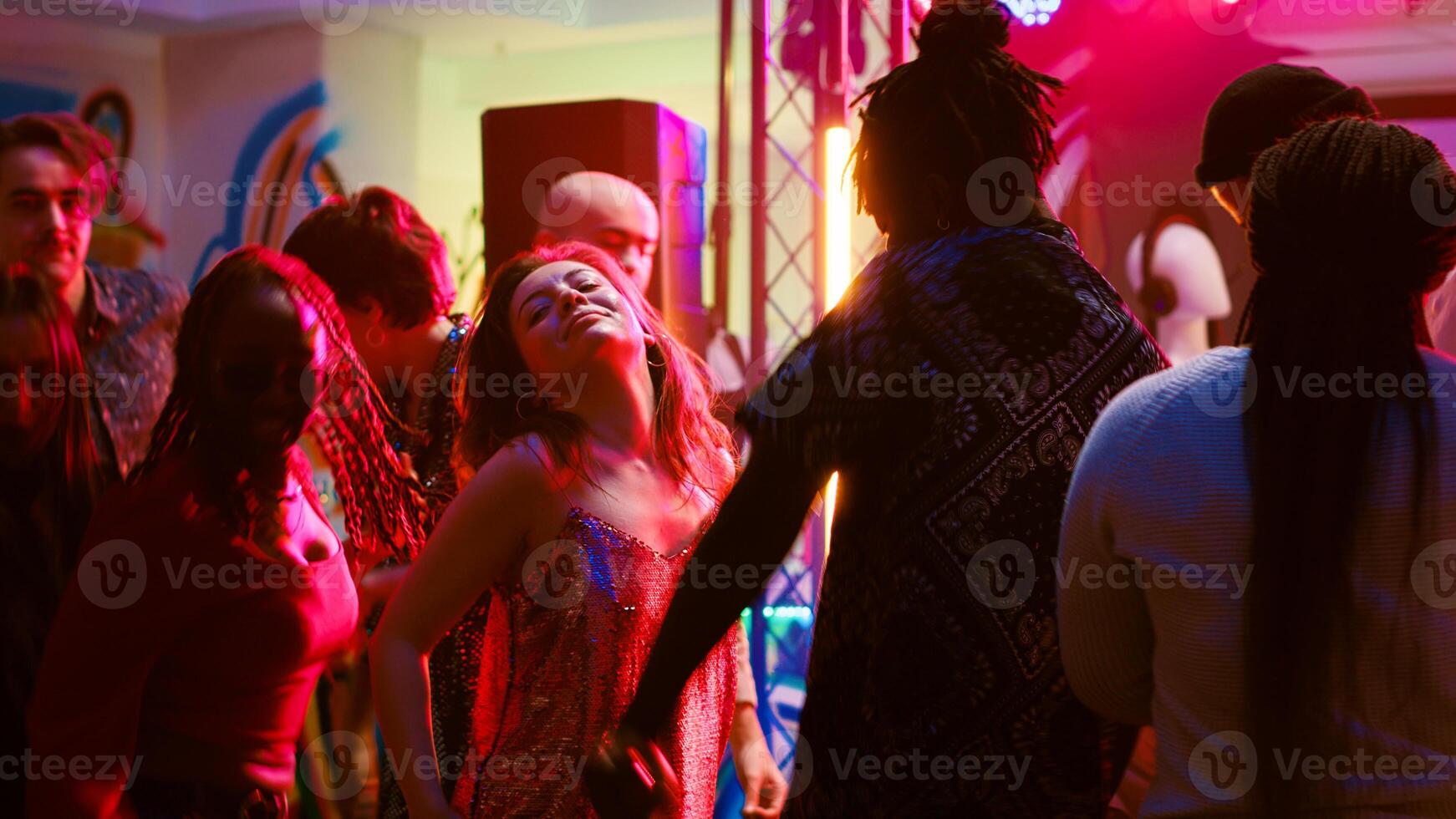 Group of friends partying together in the club, feeling happy with electronic music on dance floor. Crowd of people having fun at nightclub, enjoying party or social gathering. Tripod shot. photo