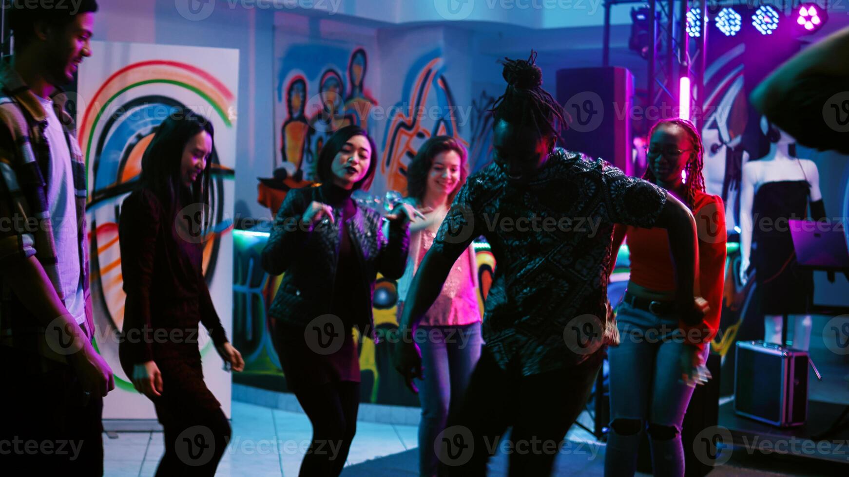 Young adults having fun partying, dancing and moving around on dance floor with stage lights. Cheerful friends doing funky dance moves having fun at underground party. Handheld shot. photo