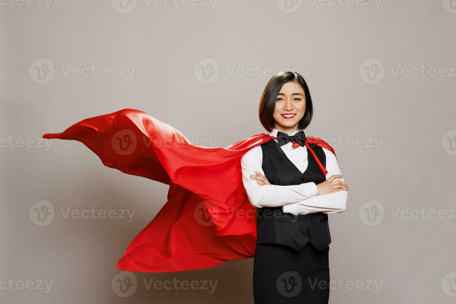 atractivo joven mujer vistiendo camarera uniforme y revoloteando superhombre capa mientras posando en estudio retrato. confidente restaurante empleado vestido en superhéroe rojo capa foto