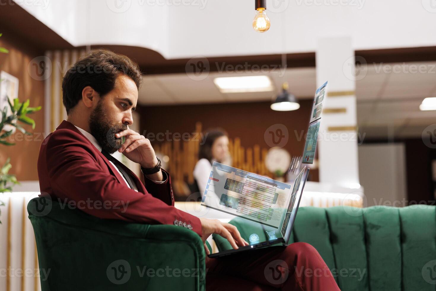 Company worker visualizing figures using augmented reality hologram, away on business trip solving accounting tasks on laptop. Employee travelling for work sitting in hotel lounge, imputing numbers photo