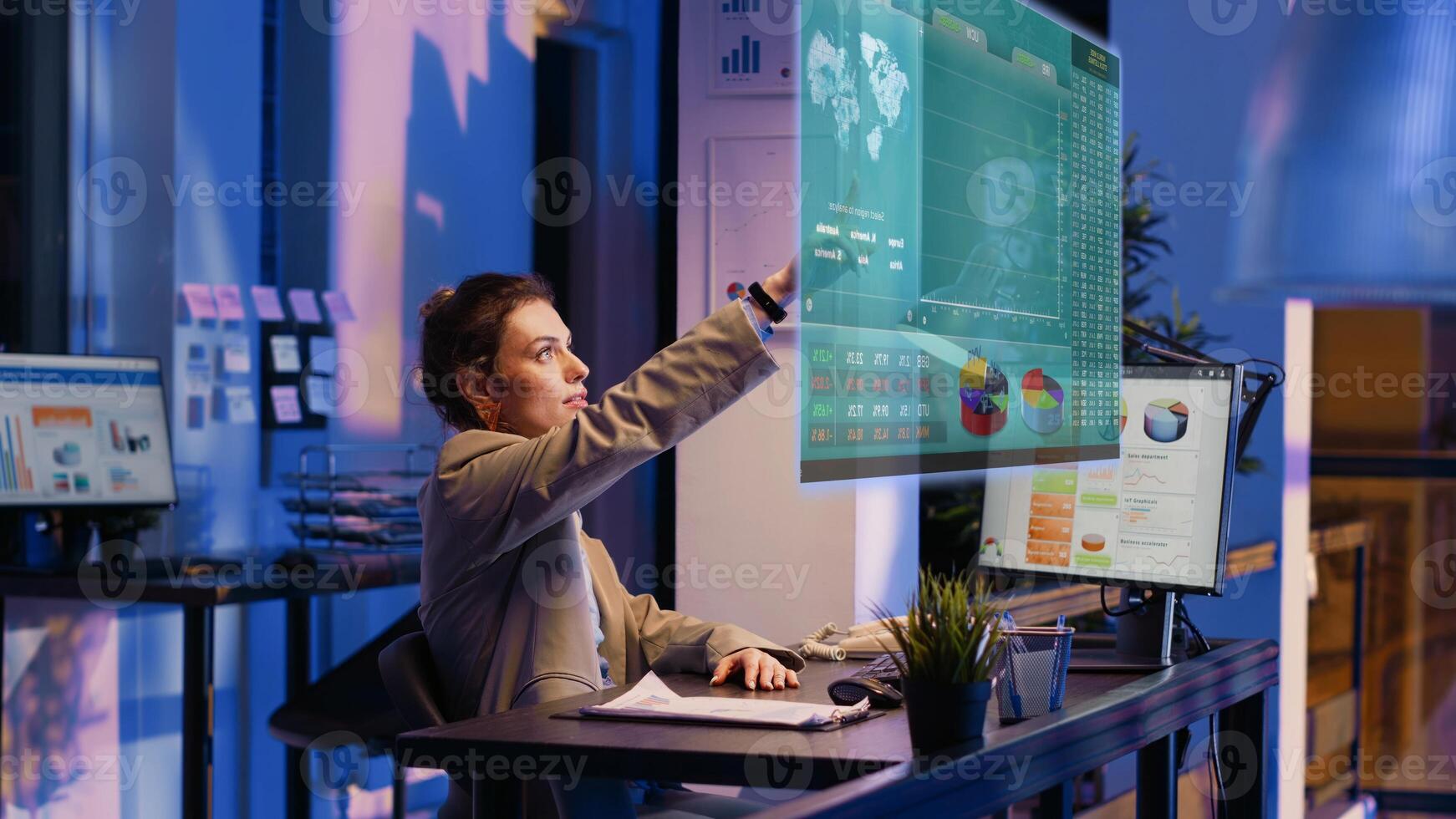 Accountant imputing revenue figures on computer in office during nightshift, visualizing them using augmented reality. Employee at desk focused on typing company statistical numbers, working overnight photo