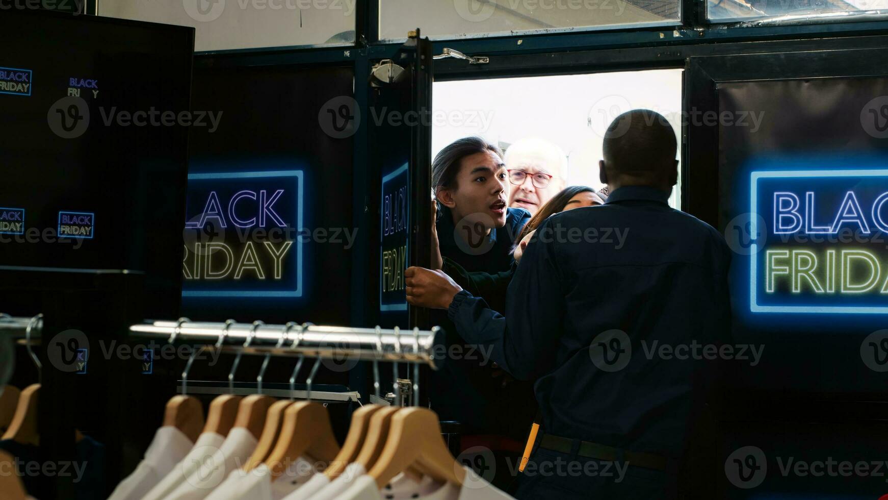 Customers demand shopping access on black friday, taking advantage of early hours to buy cheap clothes. Anxious crazy group of people pushing door and fighting with security agent. Handheld shot. photo