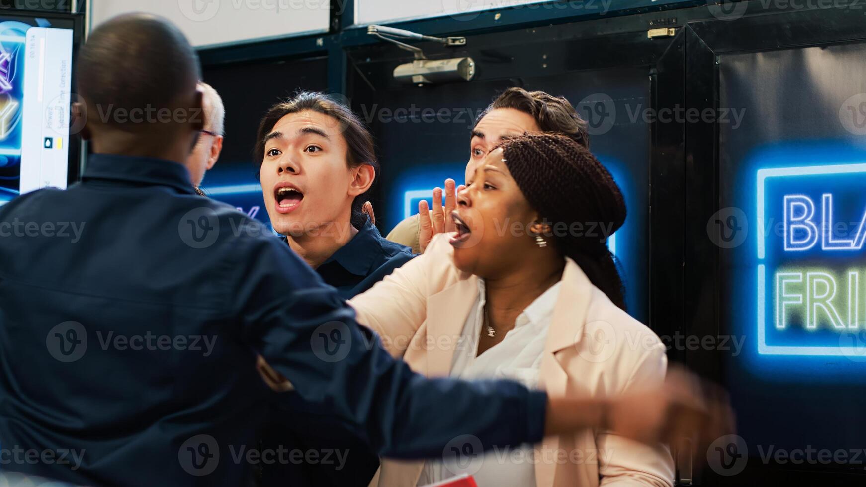 Mad diverse shoppers at store entrance going crazy for Black Friday promotions and deals, pushing through red tape. African american security agent managing crowd control during sales season. photo