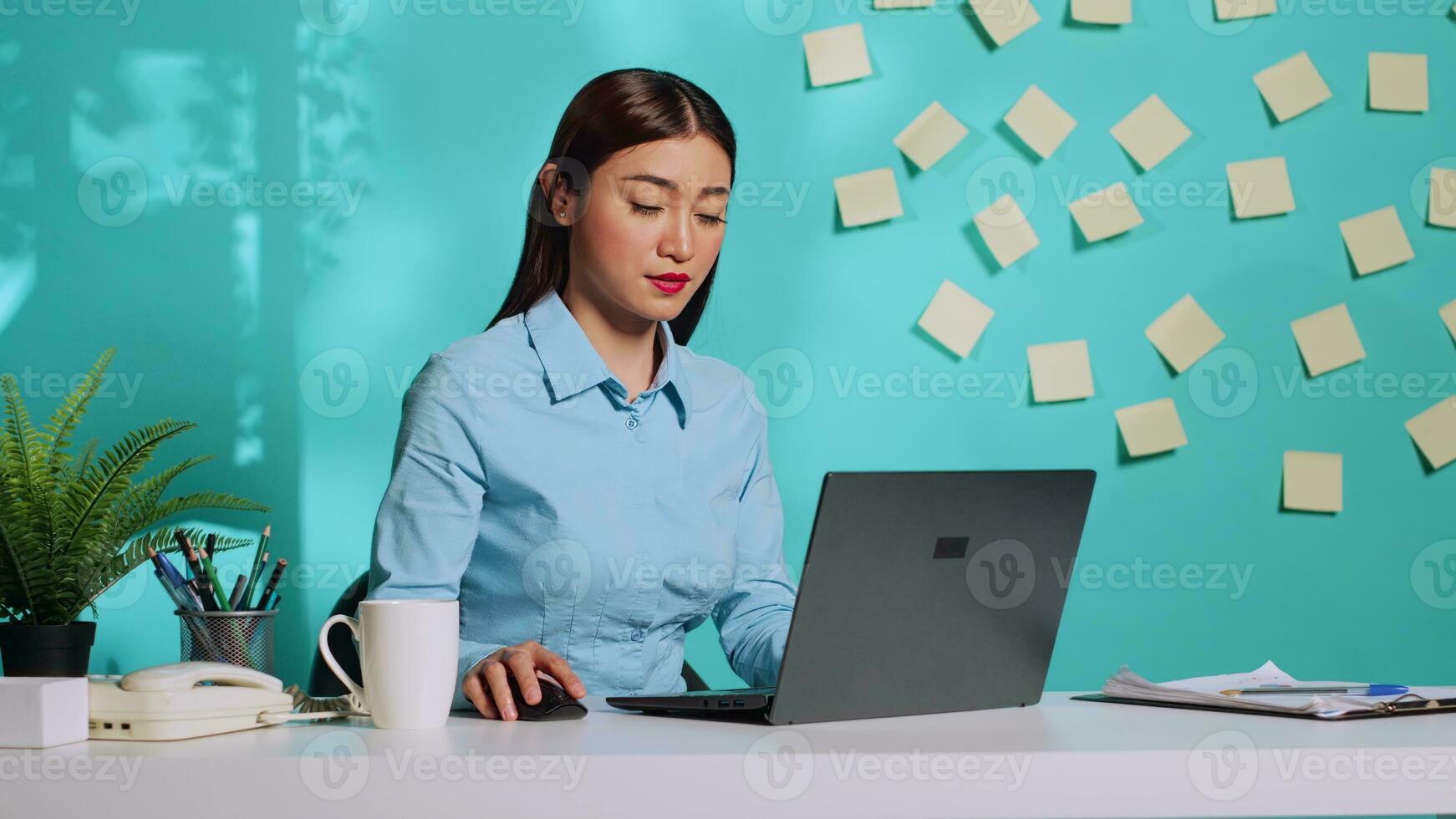 Sleepy asian office clerk woman slowly typing data after pulling allnighter. Modern bright colourful office desk in professional administration workplace over blue studio background photo