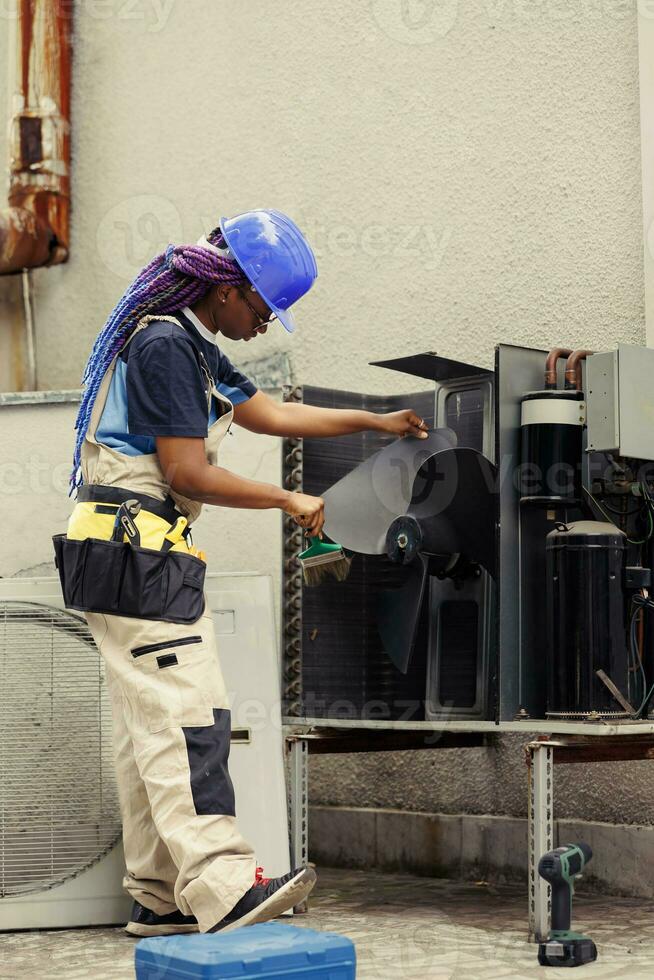 African american certified technician cleaning built up layer of dirt and dust from air conditioner internal parts to prevent reduction of cooling capacity and working capacity photo