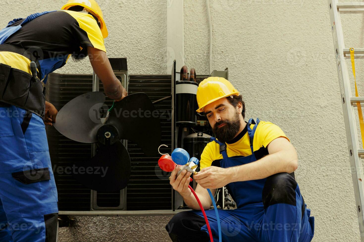 Efficient african american technician cleaning layer of dirt and dust from condenser compressor coils while coworker uses manometers to check for refrigerant leaks and read pressure in hvac system photo
