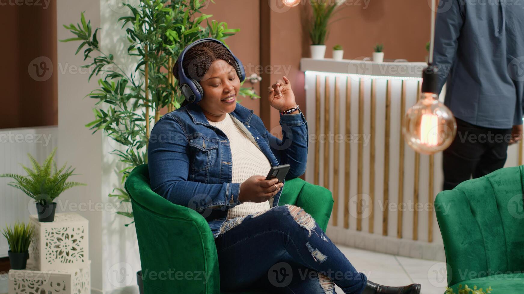 Traveller listening to music in reception lobby, having fun with audio headset and songs on smartphone. Woman waiting to do check in process at luxury hotel, sitting in lounge area on holiday. photo