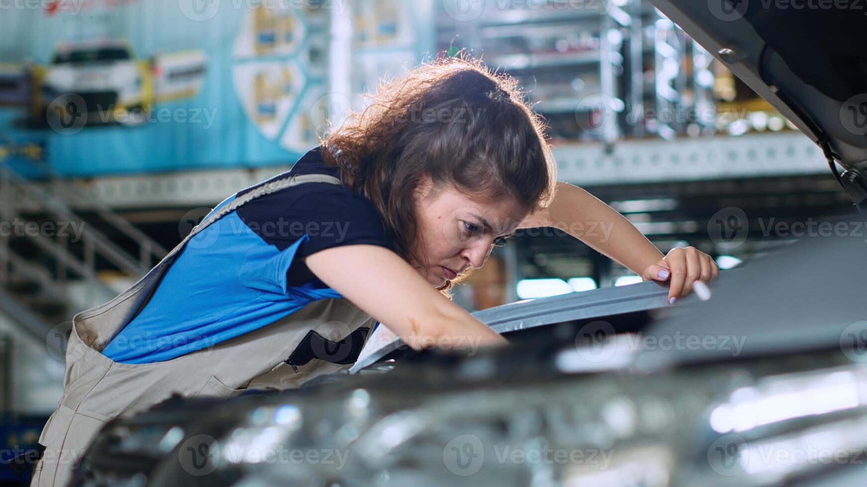 Close up shot of woman in garage using torque wrench to tighten bolts inside opened up vehicle after replacing oil. Car service employee doing inspection on automobile, wiping leftover leakage photo
