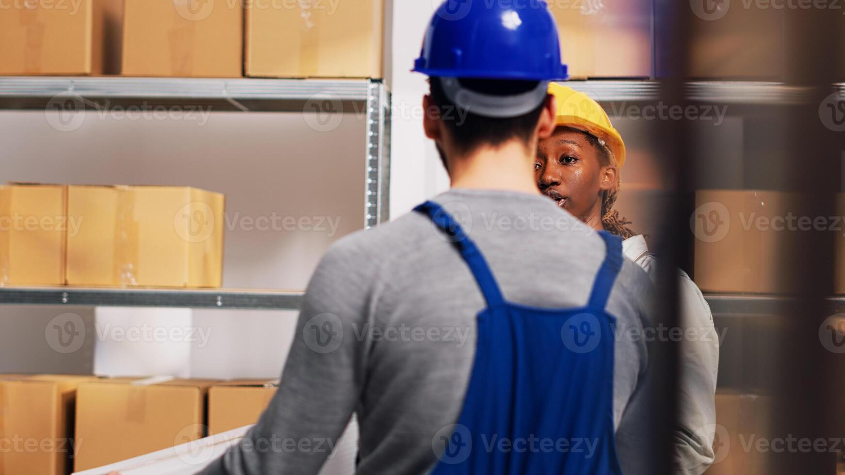 African american supervisor looking at boxes of goods in depot, checking stock logistics in warehouse shelves. Man and woman working with merchandise placed in boxes on depot racks. Handheld shot. photo