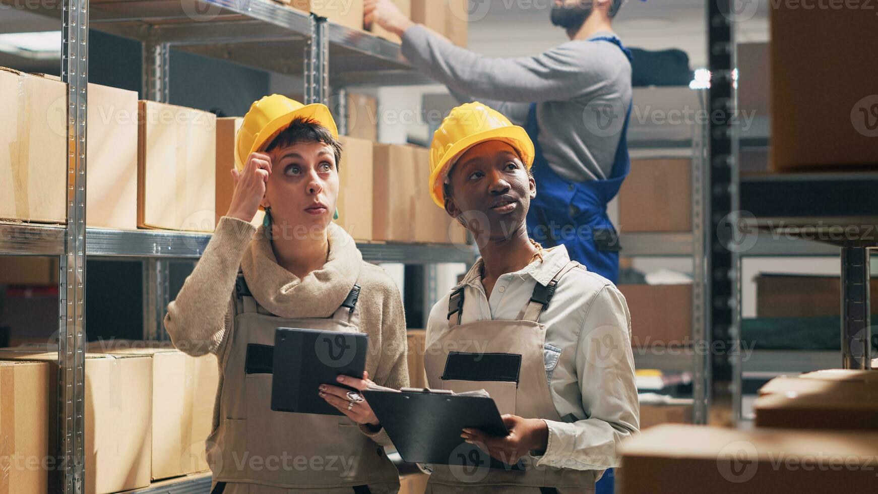 Multiethnic team of supervisors counting boxes of goods placed on warehouse racks, looking at merchandise products in packages. Young women in overalls working in storage room. photo