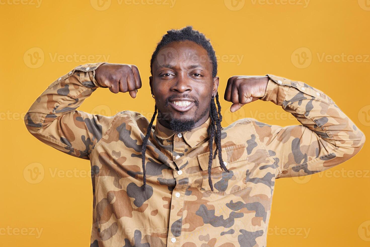 African american man flexing triceps strength before workout training in studio over yellow background. Confident athletic person posing to show biceps, muscular body from fitness photo