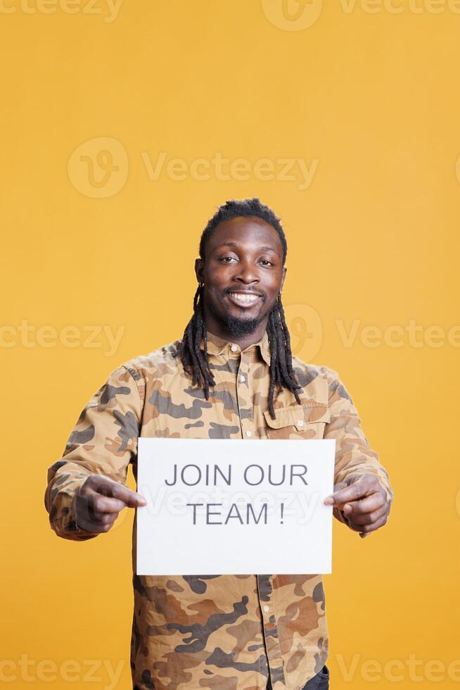 African american hr recruiter holding job offer sign, hiring candidate for business career opportunity standing in studio over yellow background. Advertisement with job application photo
