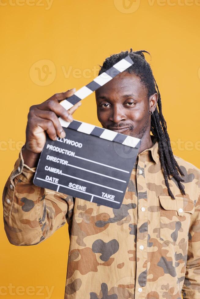 Attractive film director holding clipper board to cut scenes in movie making industry. African american man presenting chalkboard to camera and smiling while having filmmaker object. Cinema concept photo