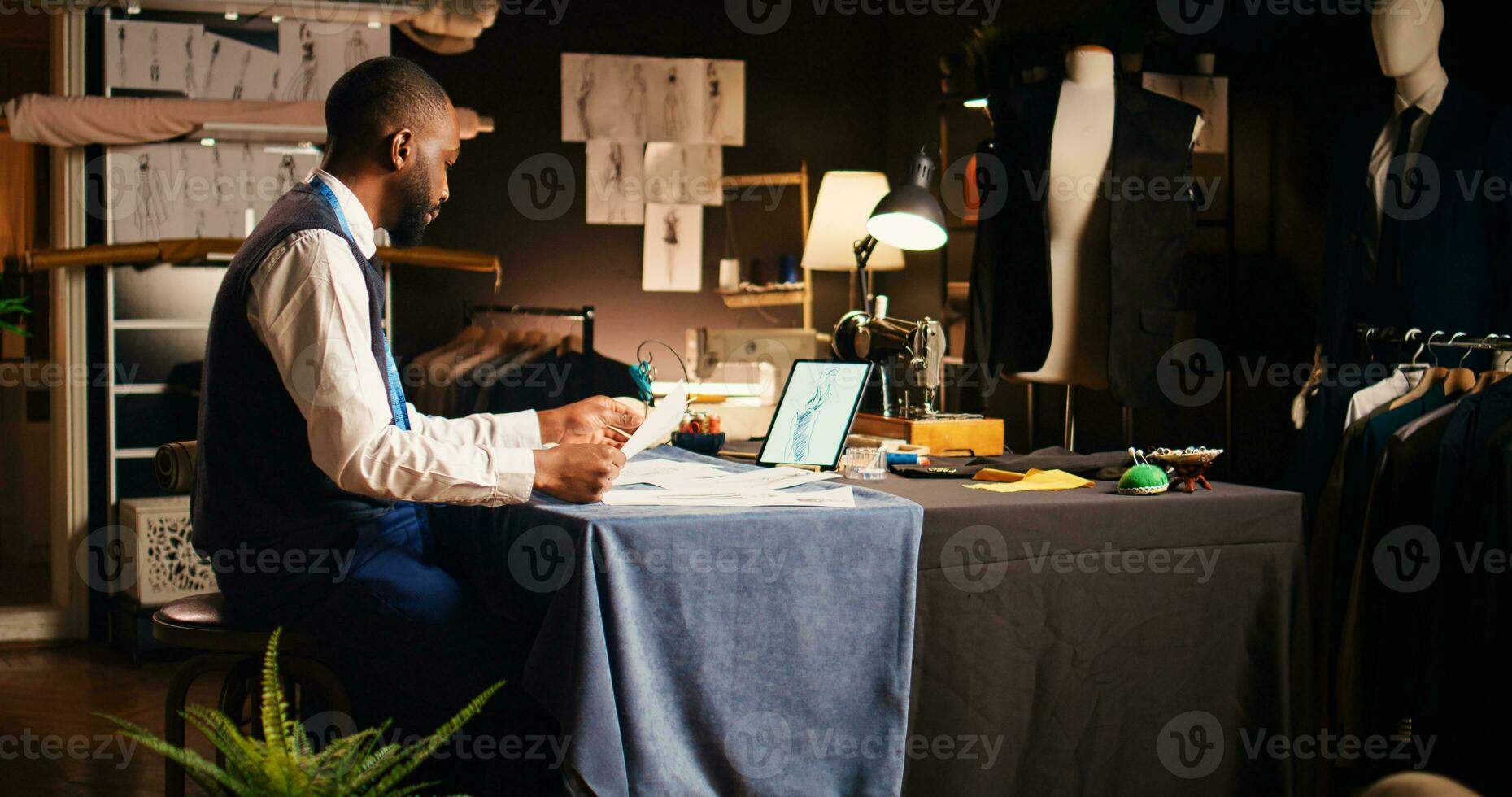 Skilled craftsman studying sketches in tailoring atelier, using outlines of clothes before creating modern clothing line. Male designer manufacturing handmade clothes, fashion concept. photo