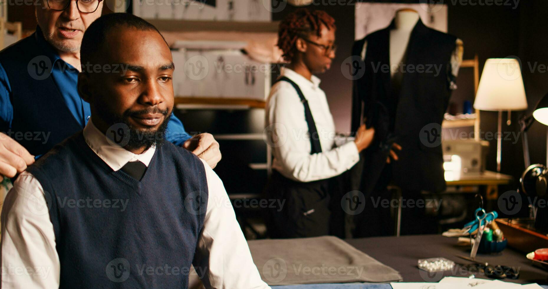 Senior craftsman taking measurements of clients body, using measuring tape to ensure perfect size for tailored suit order. Luxury atelier couturier discussing with customer about model. Handheld shot. photo