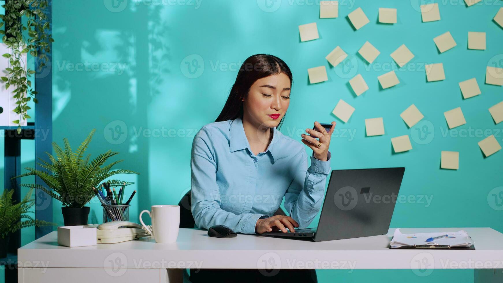 Businesswoman adding card information, managing payment method on laptop while at work. Asian employee sitting at colourful bright modern office desk over blue studio background photo