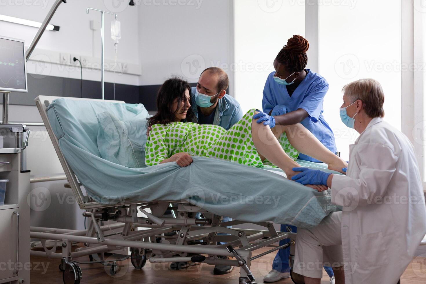 Woman pushing to give birth to baby in hospital ward, having painful contractions during caesarean surgery. Obstetrician doctor and husband comforting pregnant patient in maternity clinic photo