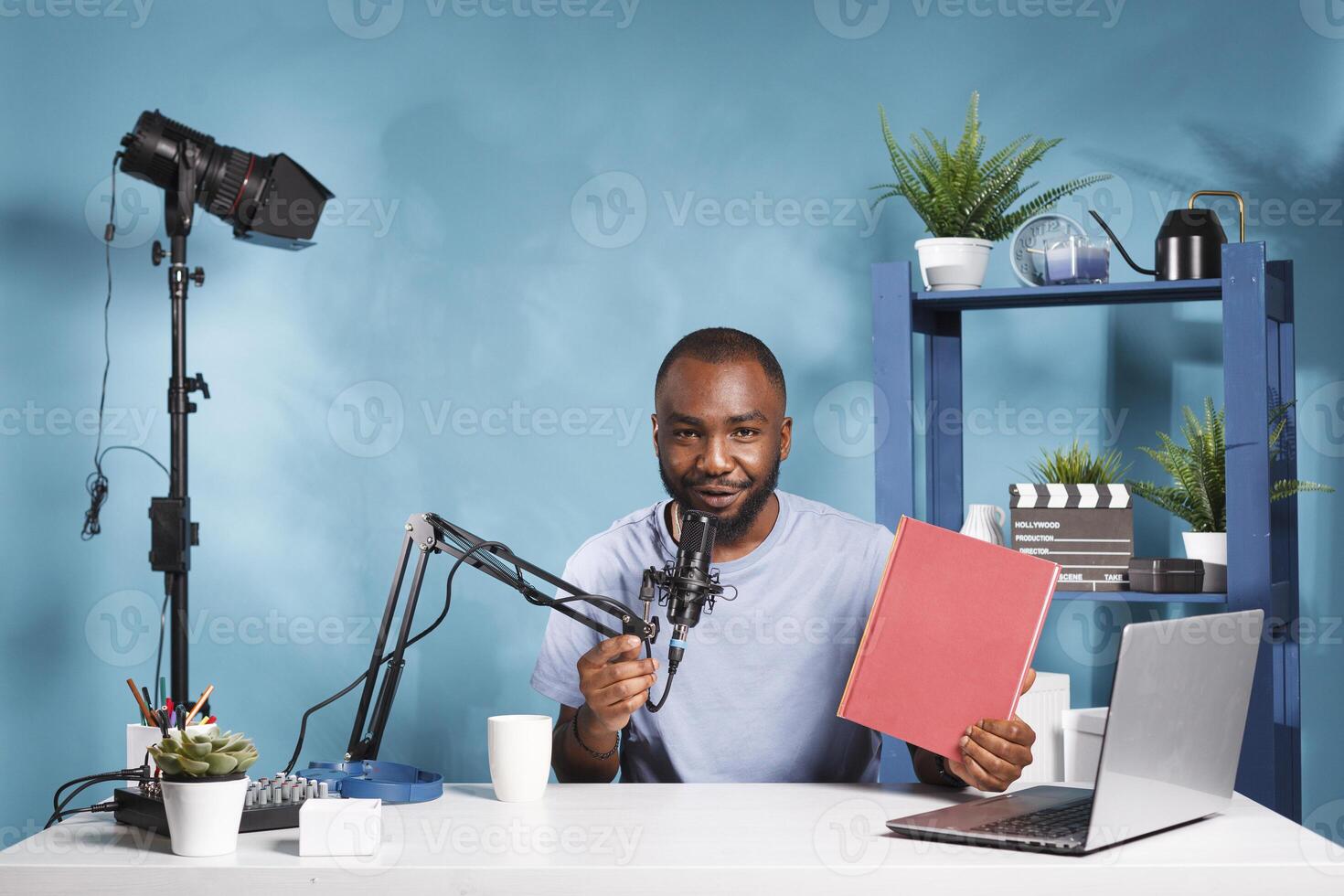 Smiling streamer presenting new book with red cover mockup and looking at camera while live broadcasting for blog. Vlogger recording novel review video for internet podcast photo