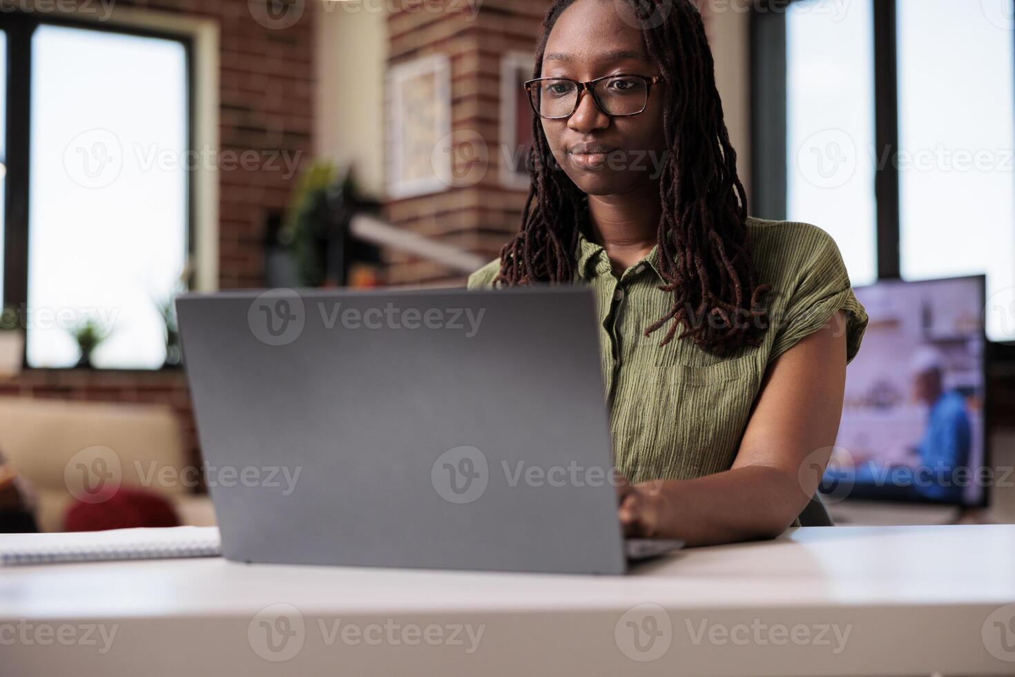 Portrait of confident freelancer looking at laptop screen and typing while working from home on business project. African american employee doing remote work on portable computer at desk in living photo