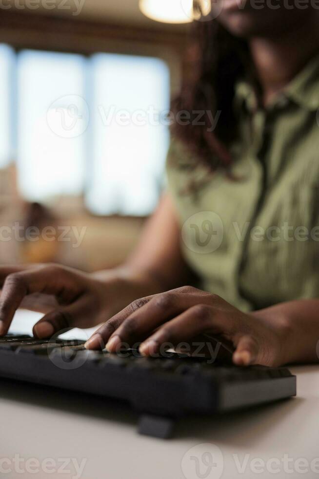 Closeup of african american student writing homework using computer keyboard while studying remote from home living room. Selective focus on woman freelancer hands typing text while chatting. photo