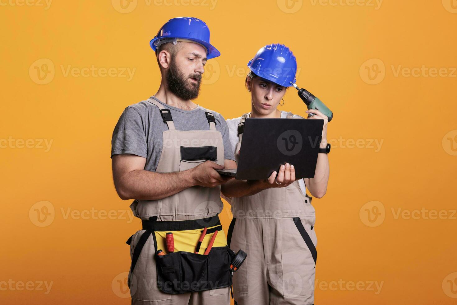 Professional builders in studio holding laptop, looking at building blueprint for new renovation project. Renovators wearing renovating uniform making decisions together as team. photo