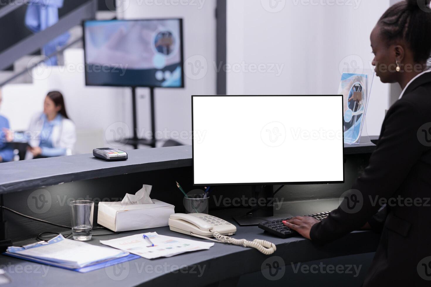 African american receptionist using white isolated screen on computer while working at hospital registration counter. Reception worker looking at mockup template during checkup visit appointment photo