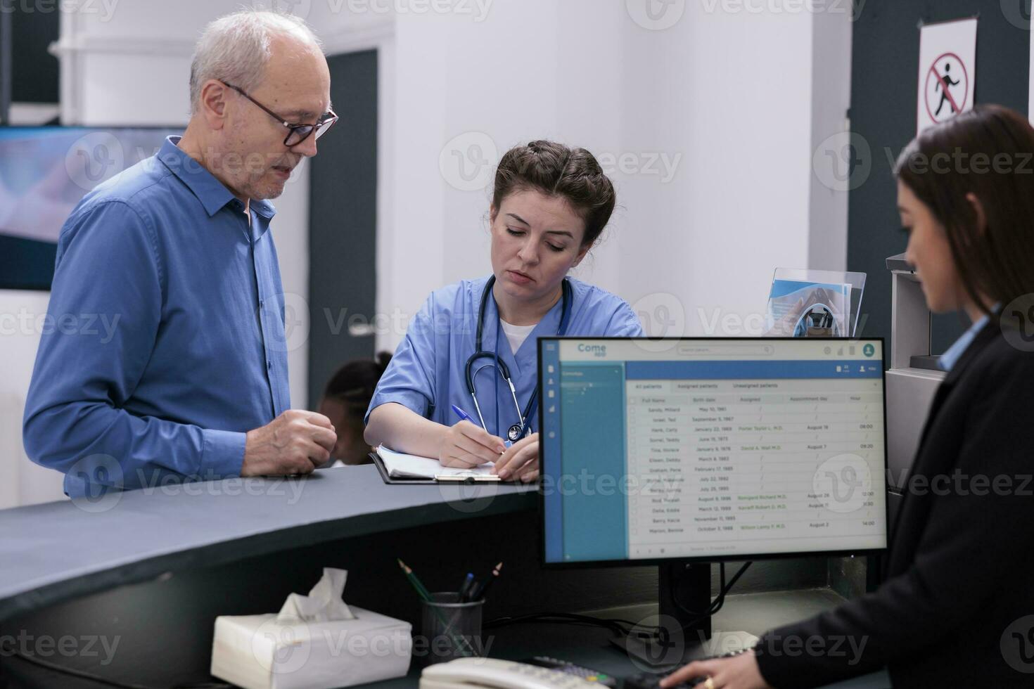 Nurse looking at medical report with elderly patient while signing documents before start examination in hospital waiting room. Senior man having checkup visit with doctor, health care service photo