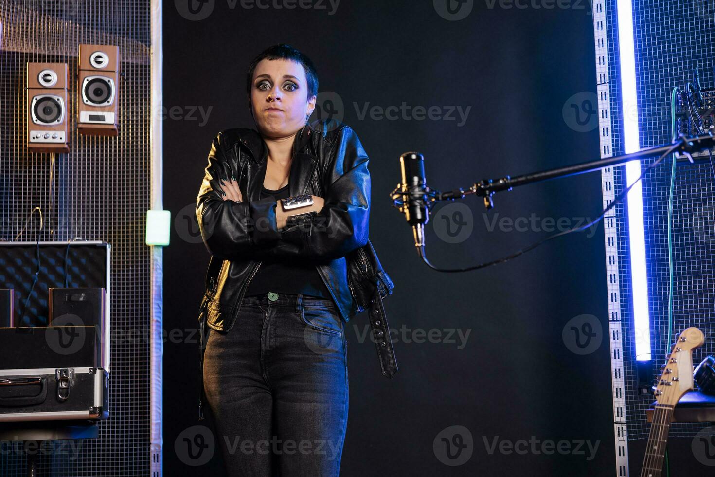 rock músico haciendo yo no saber gesto mientras en pie en frente de micrófono preparando a canta pesado metal canción, trabajando a grunge álbum. artista jugando punk música utilizando instrumento electrico foto