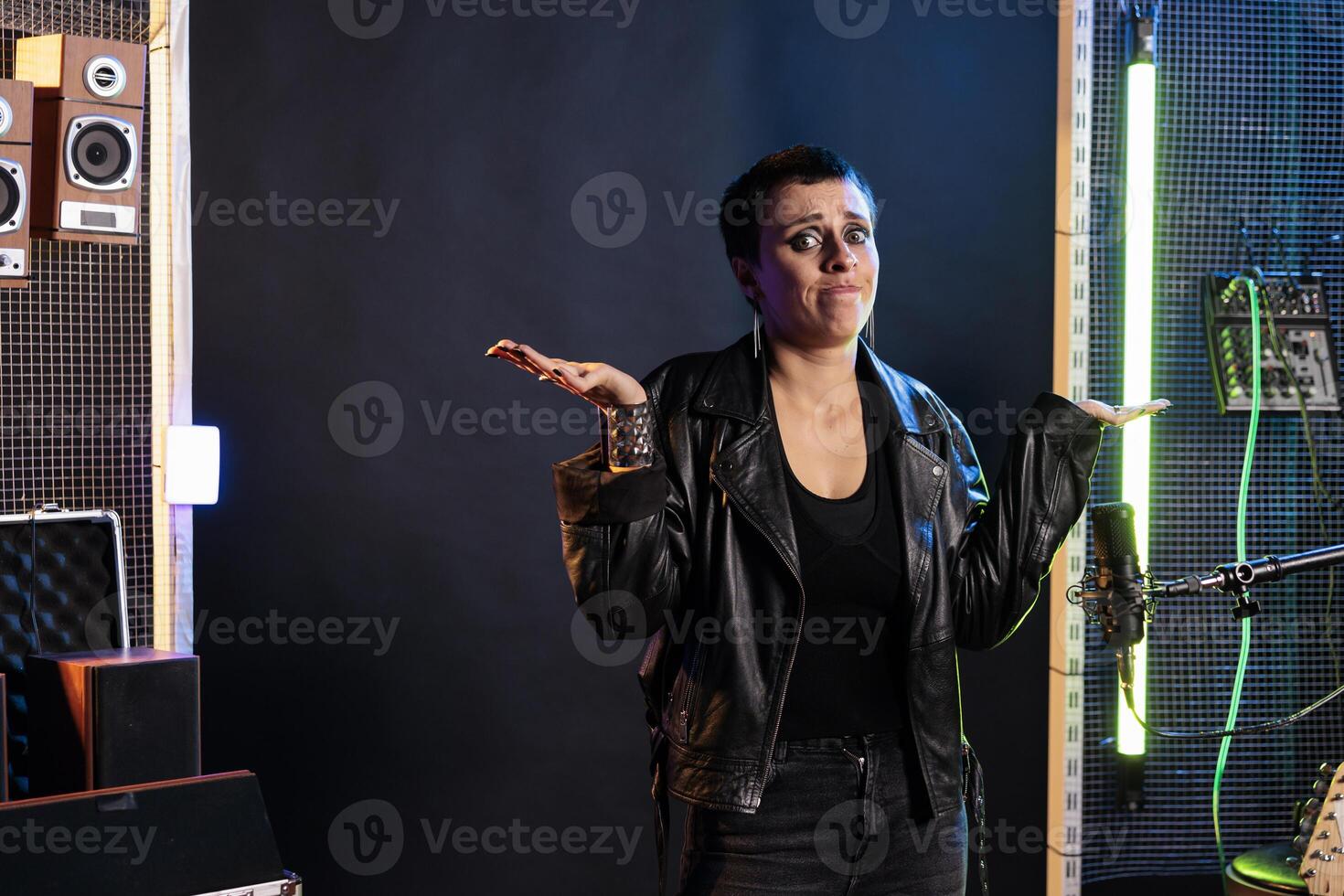 Confused punk superstar having uncertain expression while standing in sound studio while working at rock album, preparing heavy metal song using electric guitar. Dont know gesture concept photo