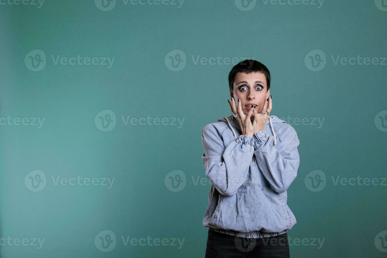 Afraid nervous woman having terrified expression after hearing the news, terrified person standing in studio posing over isolated background. Frightened female looking at camera with shock reaction photo