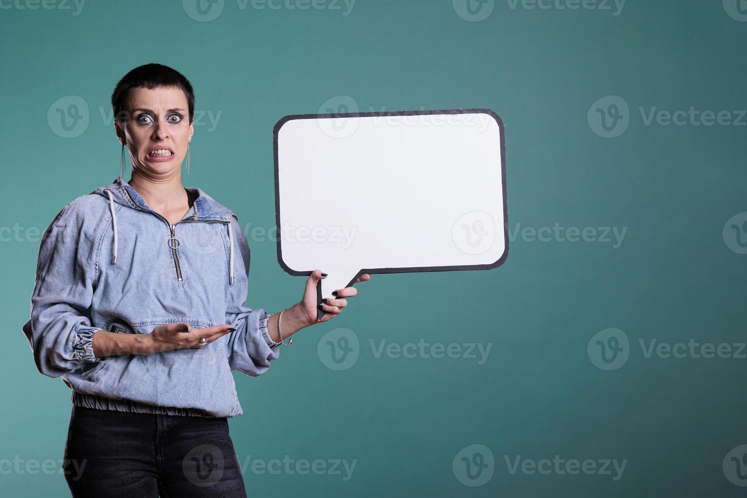 Woman showing white placard with copy space for advertisement in studio, standing over isolated background. Cheerful confident brunette model with blank sign for communication on board photo