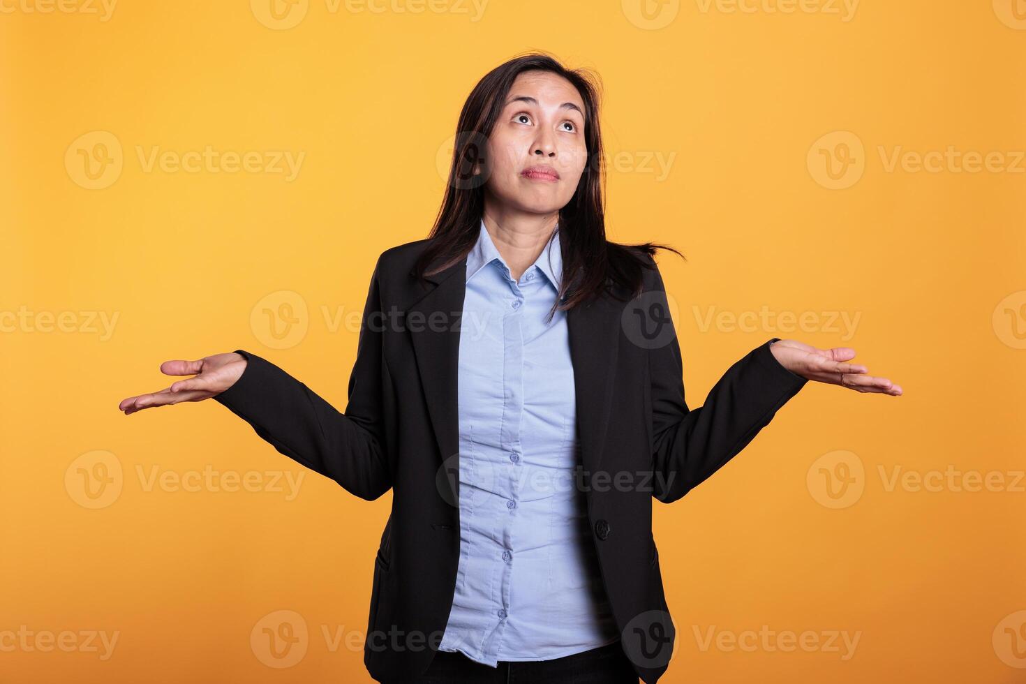 Asian woman shrugging shoulders doing i dont know sign, having doubtful facial expression in studio. Uninterested confused adult feeling clueless and puzzled about question answer. photo