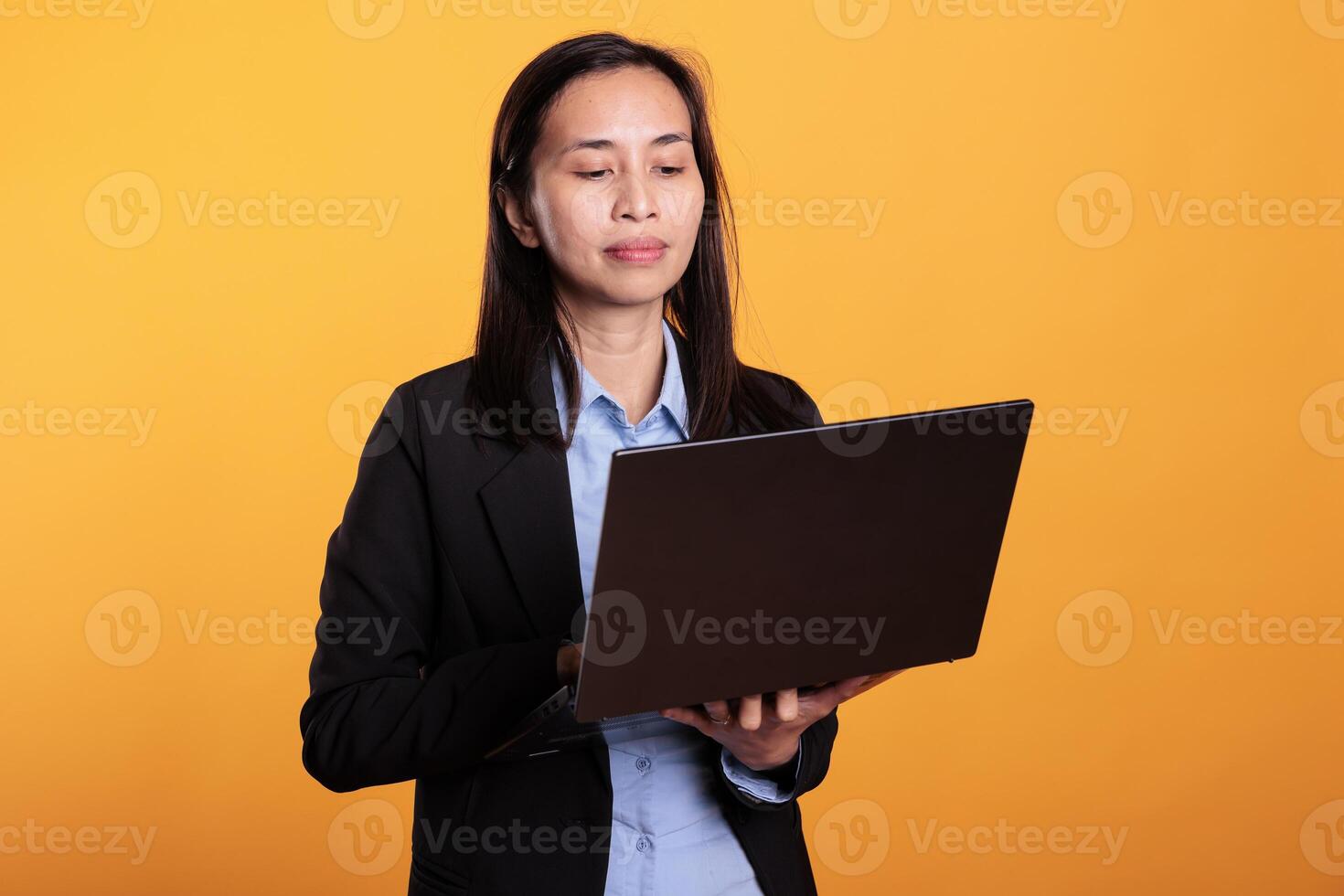 Asian woman holding laptop computer browsing on website, working at research project in studio. Positive model searching information on internet, using device to scroll through social media app photo