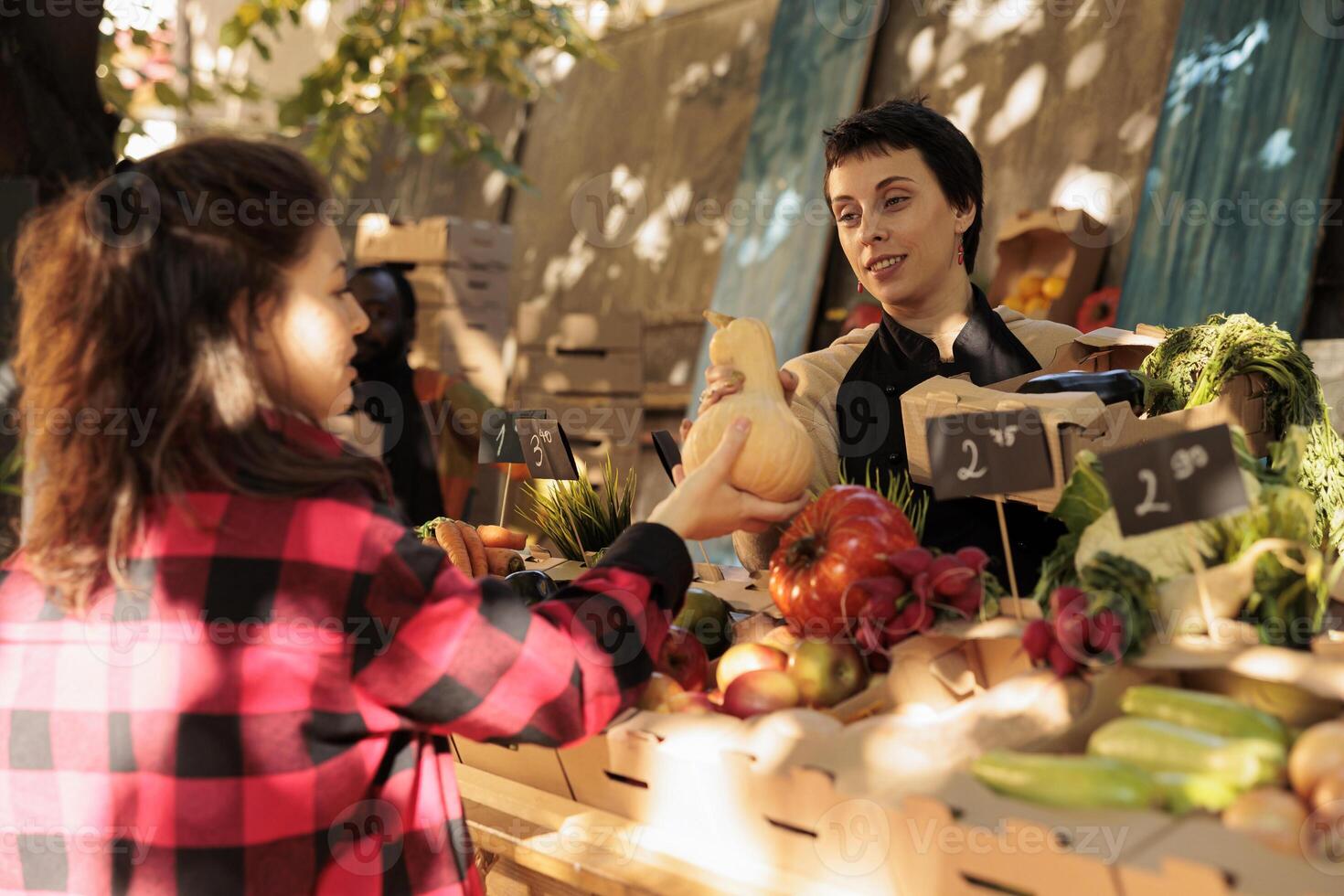 Female stall holder selling fresh organic bio products on stand, talking to customer about healthy eating and local natural veggies. Young woman asking small business owner about eco produce. photo