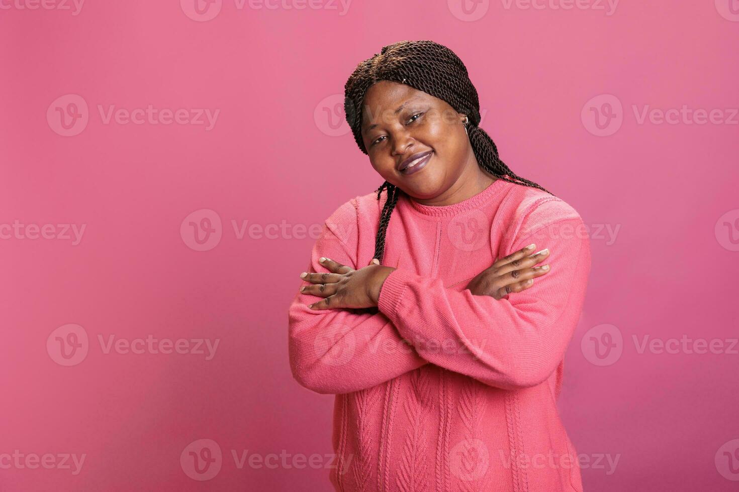 Portrait of happy woman smiling with confidence while posing in studio having cheerful expression enjoying shoot time. African american model with stylish hairstyle and pink sweather looking at camera photo