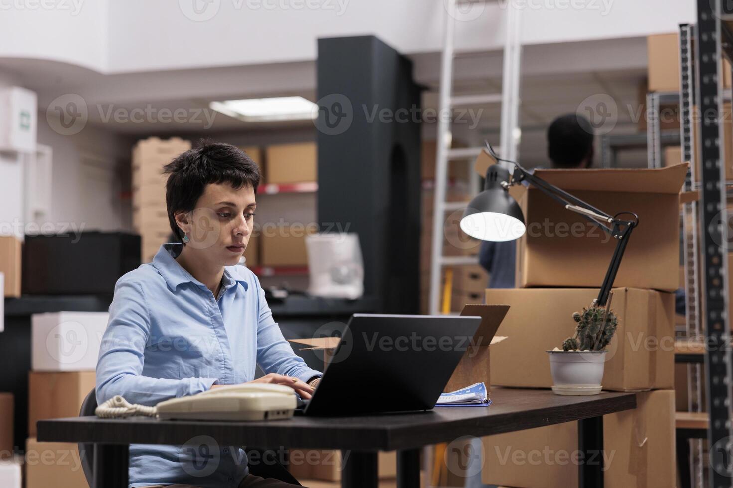 Storehouse employee looking at cargo stock on laptop computer while checking shipping detalies before start preparing customers packages. Worker working at warehouse delivery department photo