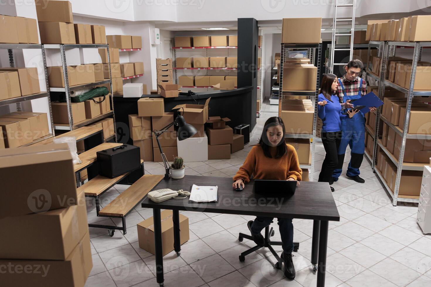 Warehouse asian employees team preparing order parcel for shipment in retail business storage room. Storehouse workers analyzing goods checklist and creating invoice on laptop photo