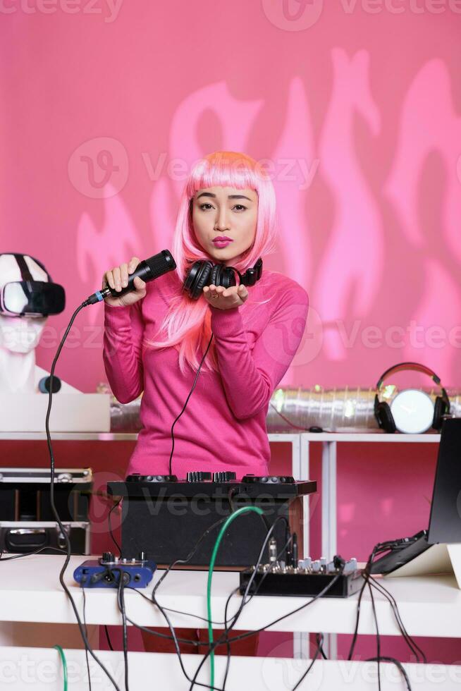 Lovely dj performer blowing air kisses while mixing eletronic music with techno using turntables, having fun during performance. Attractive artist with pink hair performing in club at night photo