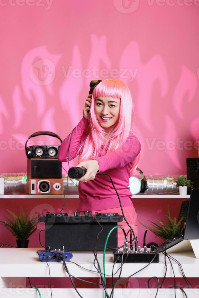 Asian musical artist playing electronic music using mixer console while hold out the microphone to fans, enjoying dacing together and having fun. Dj woman performing at night in club photo