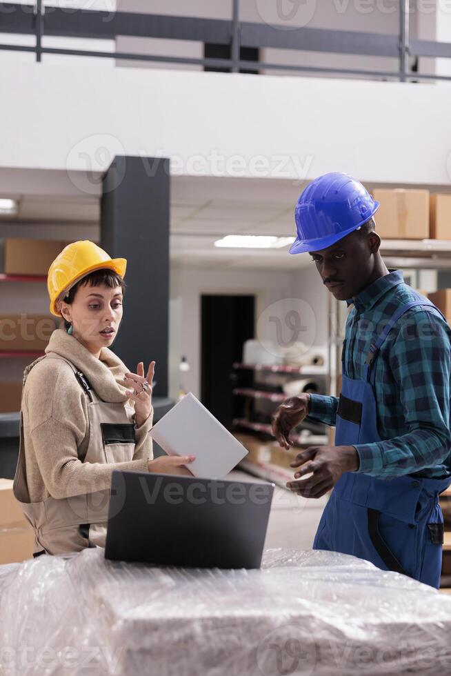 Storehouse managers reading order goods checklist on laptop, choosing cardboard box for packing in warehouse. Man and woman ecommerce store stockroom workers preparing parcel for shipping photo