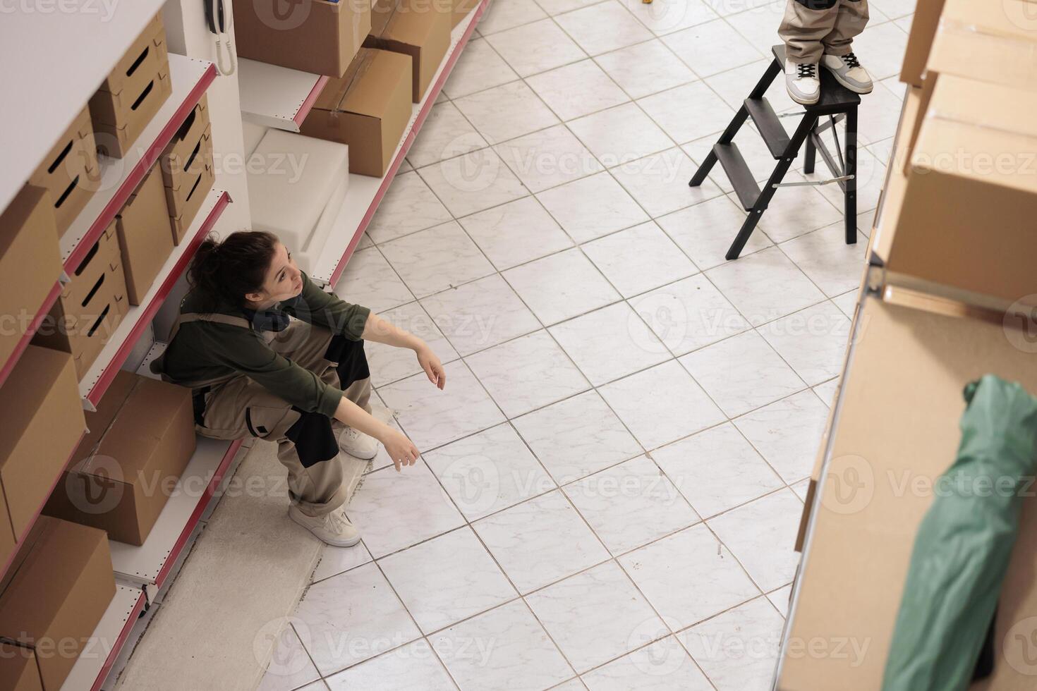 Top view of warehouse employee standing on shelf in storage room, taking a break before start working at inventory. Small business worker preparing customers orders in storehouse photo