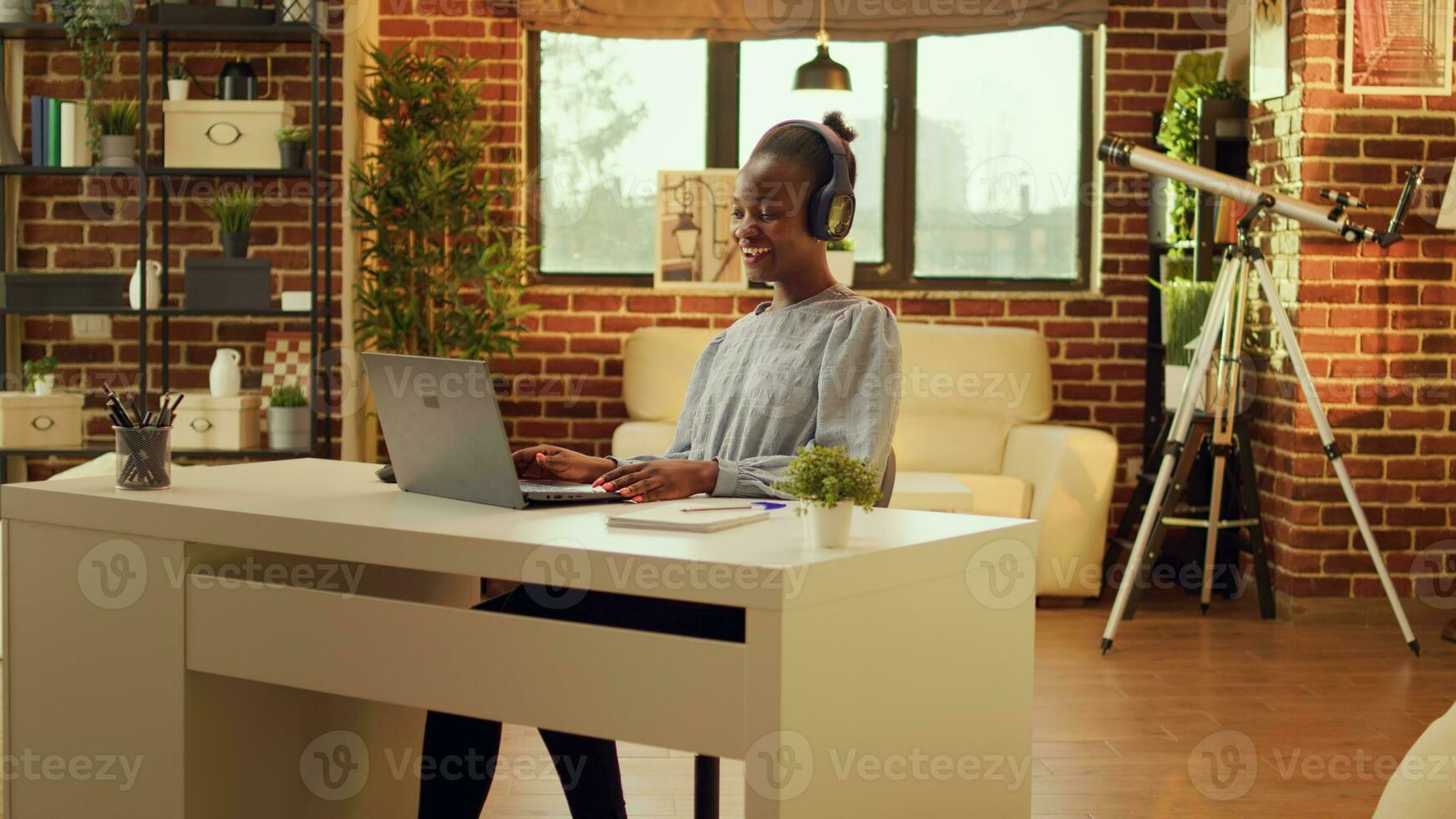 Relaxed woman listens to music, typing information on laptop at workstation. African american teleworker creating online career, enjoying remote job at home office while singing songs. photo