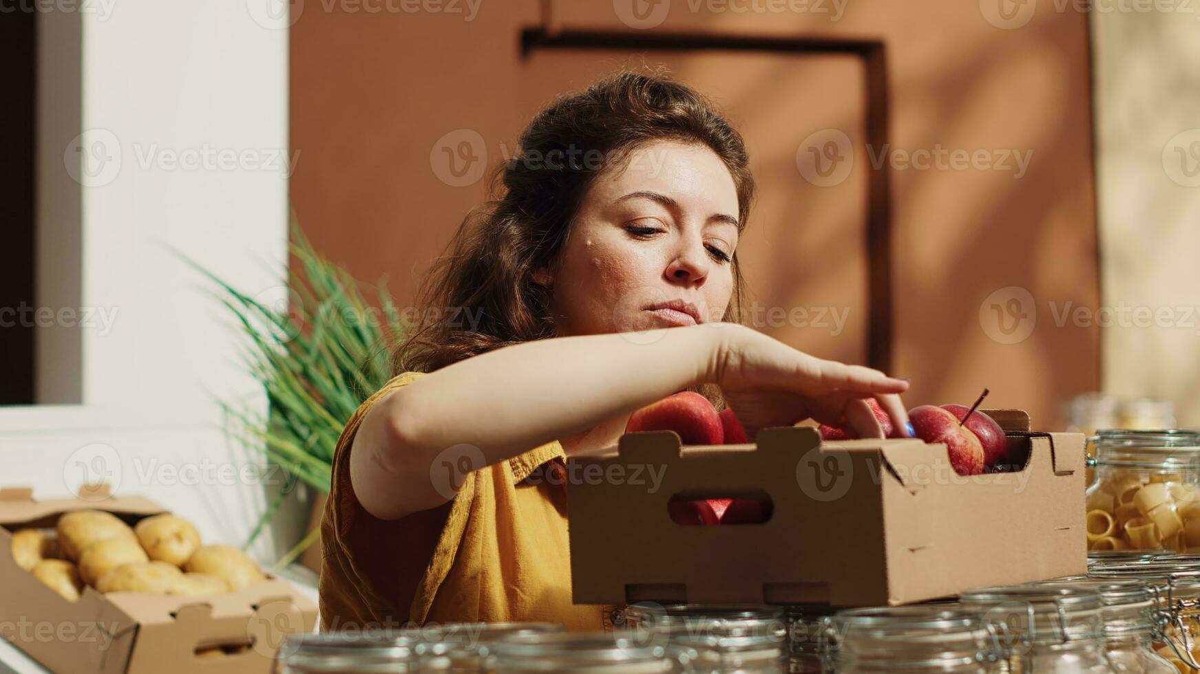Vegan woman in sustainable zero waste supermarket smelling apples before adding them to shopping basket. Client in local neighborhood grocery shop picking locally grown fruits photo