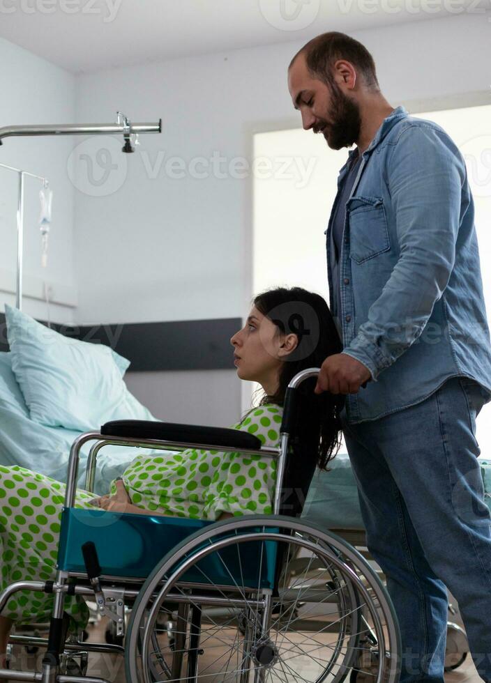 embarazada mujer sentado en silla de ruedas mientras futuro padre tomando su a maternidad habitación preparando para niño entrega en hospital pabellón. joven Pareja consiguiendo Listo para parto, que se discute paternidad foto